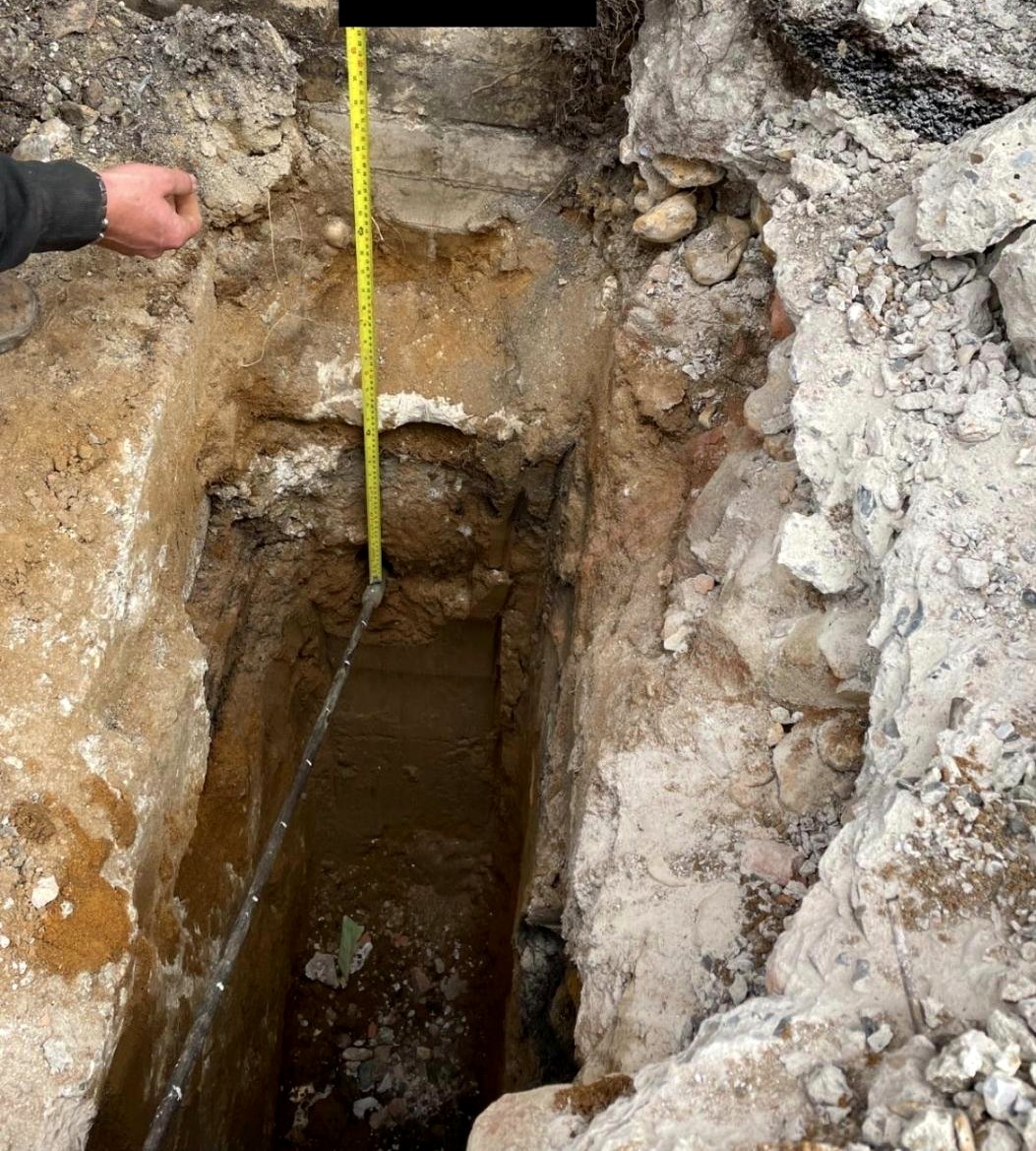 Hand-dug trial pit with tape measure